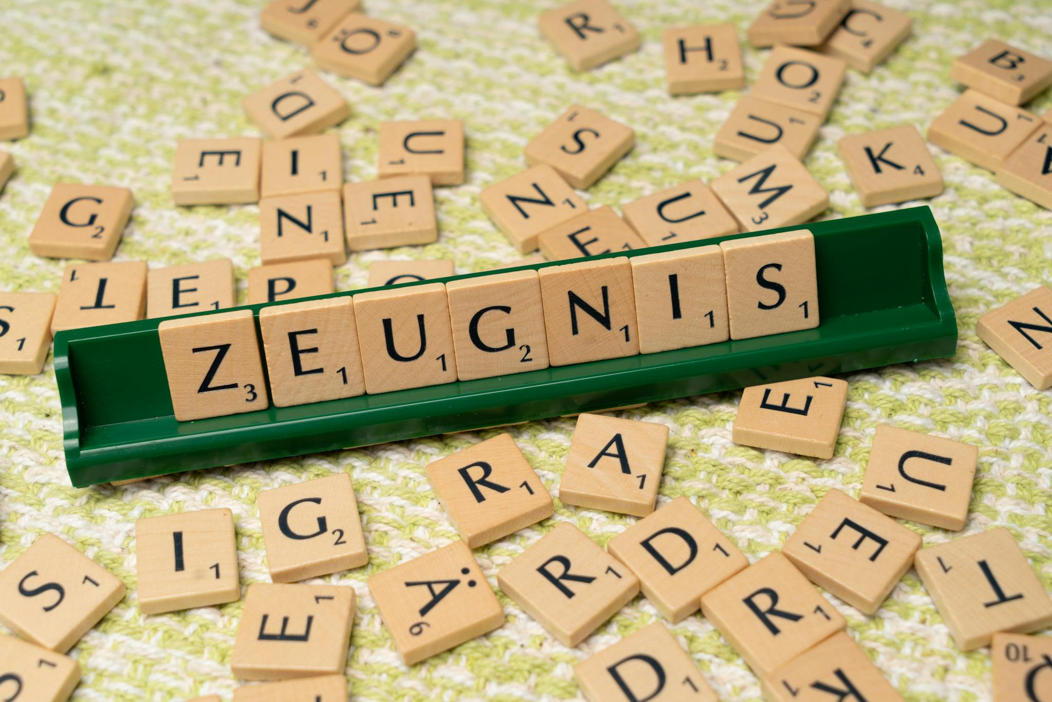 Wooden letter tiles arranged to spell 'Zeugnis' on a green tile holder, creative wordplay concept.